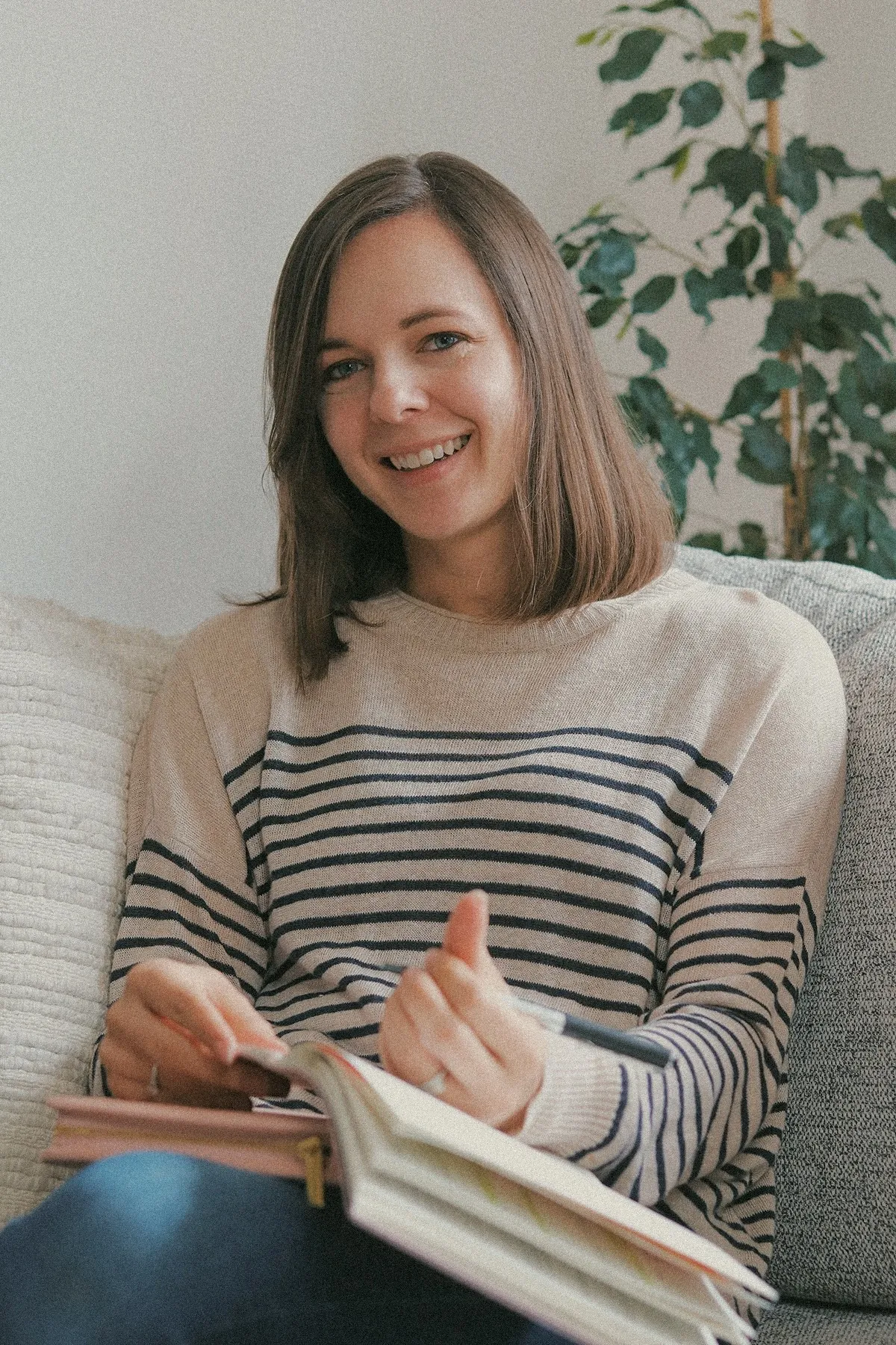 Charlotte Ellis smiling on a sofa with a notebook and pen